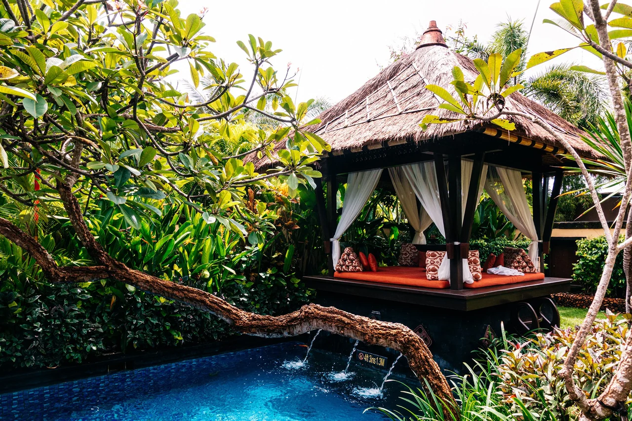A thatched daybed pavilion beside a private plunge pool in a tropical garden