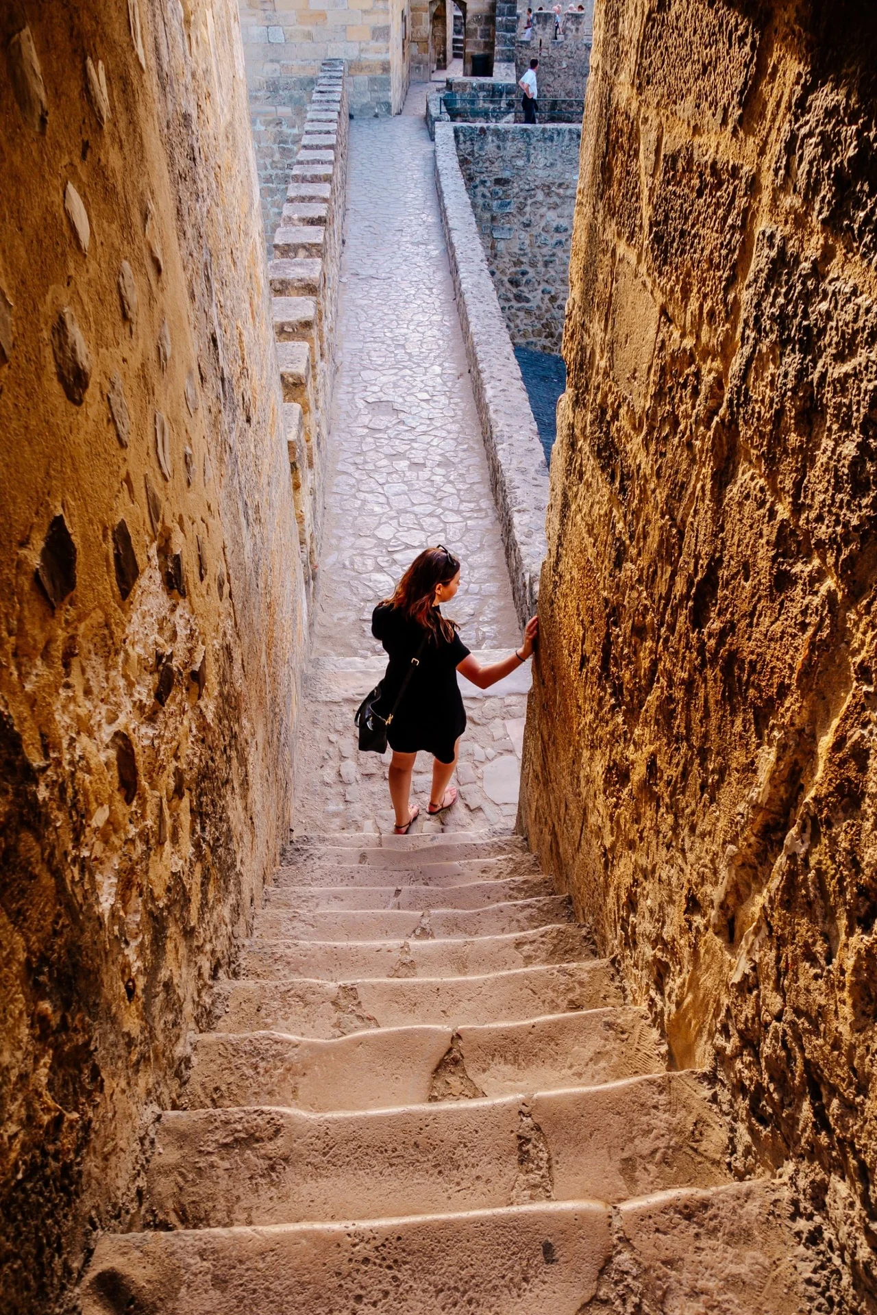 Gina descending worn stone steps between the golden walls of a castle in Lisbon