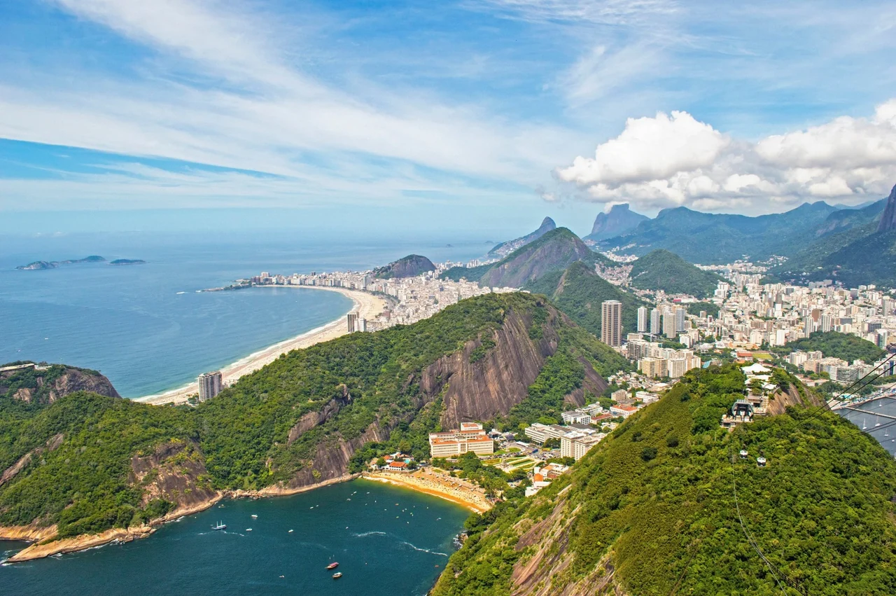 Copacabana Beach curving below green peaks, seen from above Red Beach and Urca in Rio de Janeiro