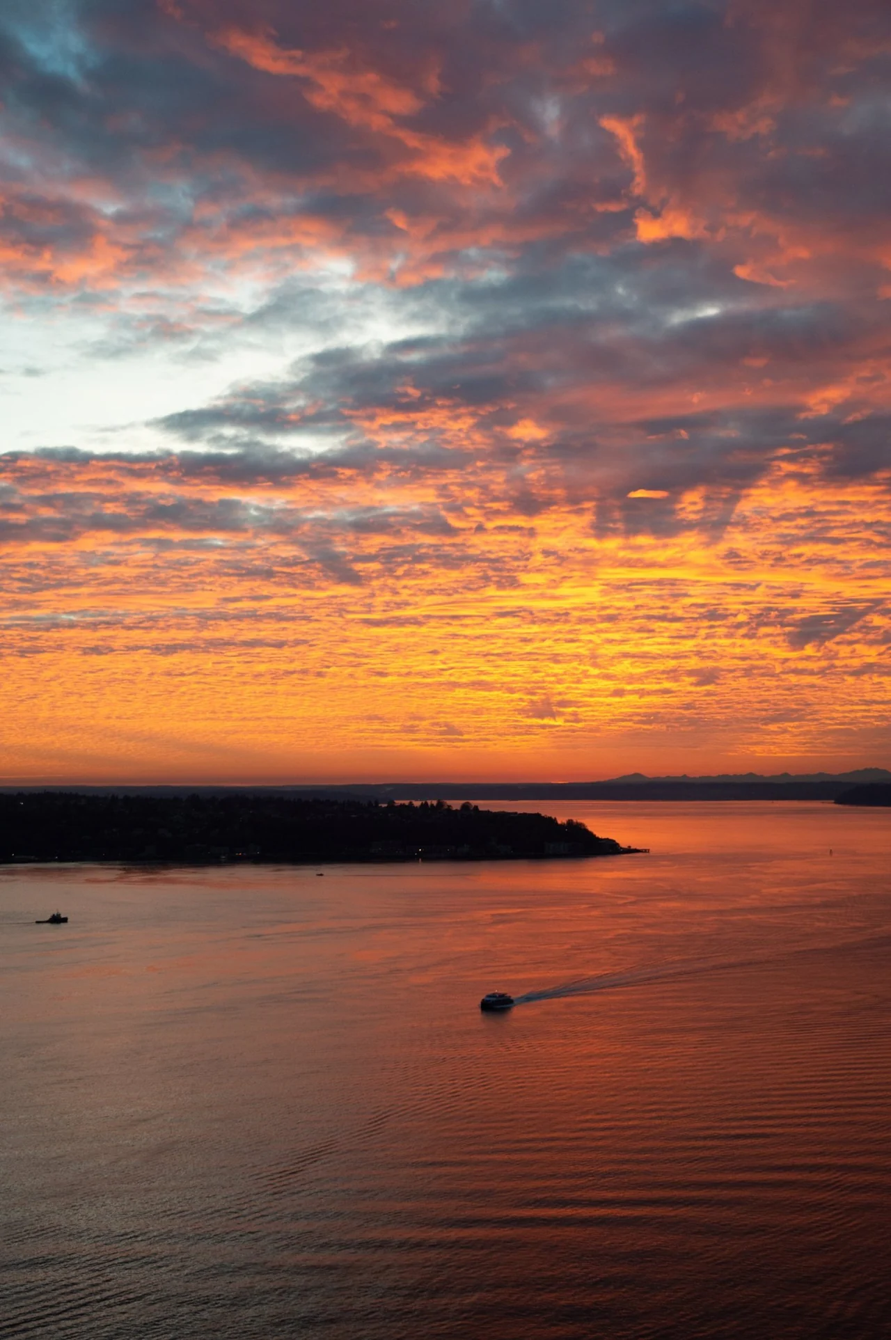 A ferry crossing a glowing orange Puget Sound under a fiery sunset