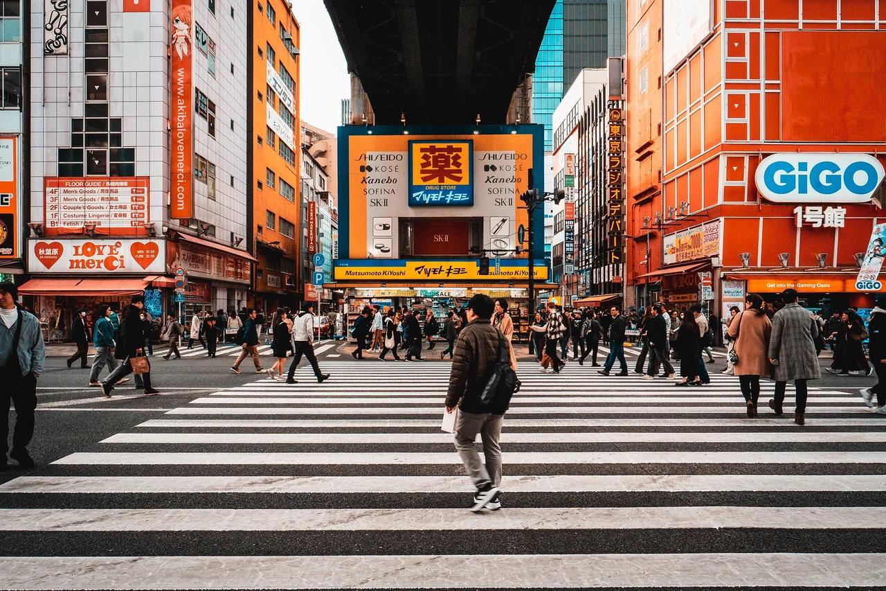 Pedestrians crossing a wide crosswalk beneath bright storefront signs