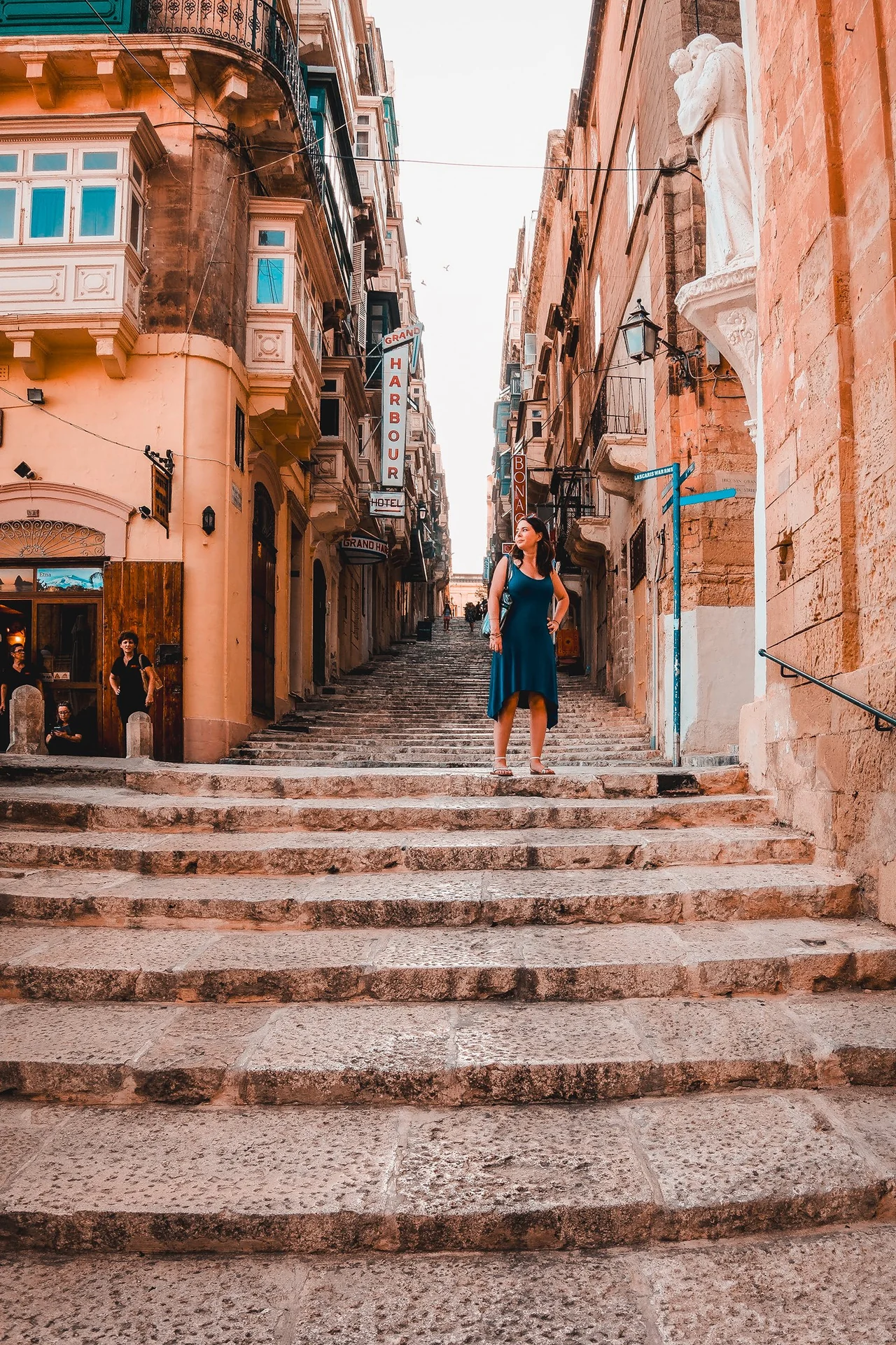 A traveler on worn limestone steps between golden buildings with enclosed balconies
